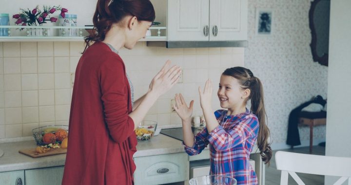 Happy young mother and cute funny daughter playing clapping hands game and have fun while cooking in kitchen at home. Family, cooking and people concept